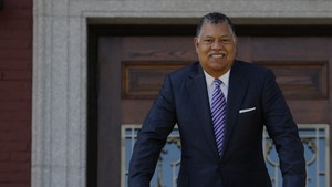 A portrait of Holy Cross President Vincent D. Rougeau leaning on a railing and smiling. 