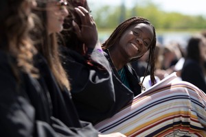 A student leans forward and smiles at the camera while seated during commencement exercises.