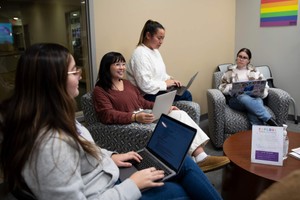 Four female students interacting while seated with laptop computers in their laps.