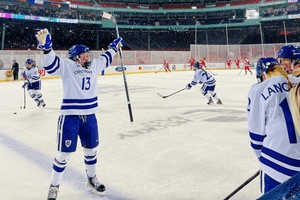 A hockey player raises her arms in excitement while on the ice at Fenway Park in Boston, MA.